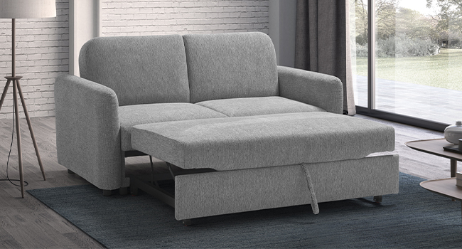 Canapé gris moderne avec fonction gigogne ou extensible, visible contre des vitres. Démontre une fonctionnalité convertible de la position canapé à la position chaise longue.