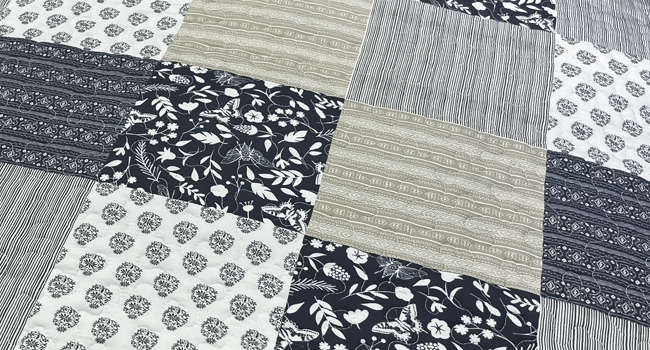 Motif patchwork de divers tissus gris et blancs présentant différents motifs géométriques et floraux disposés en blocs carrés pour créer une texture matelassée.